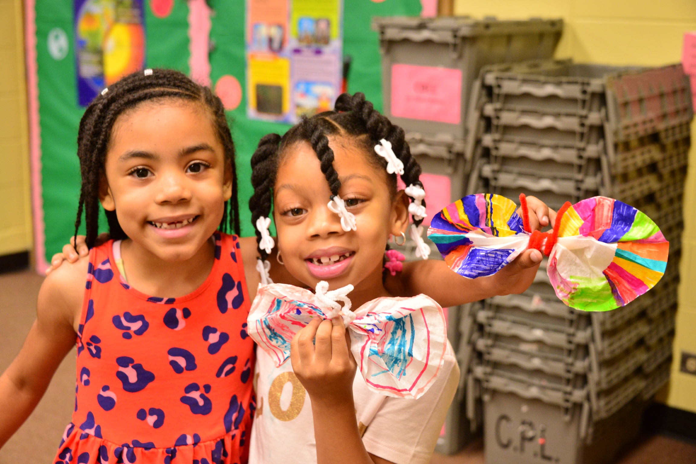Two smiling young girls holding art projects